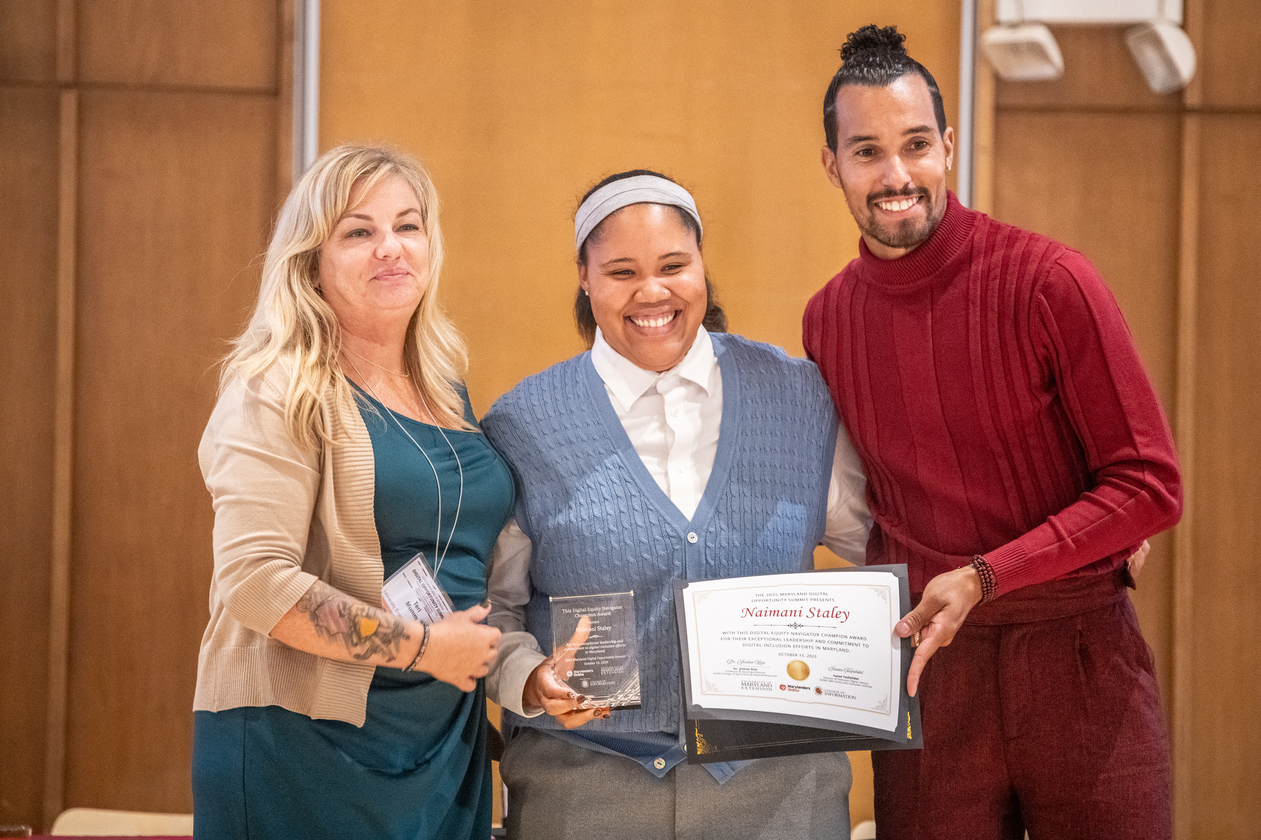 aimani Staley, Tech Extension Educator, stands to accept the Navigator Champion Award from  Teri Mumm, Digital Navigation Program Manager, UME Marylanders Online (left) and Ronnie Hammond, Director of the Maryland Office of Statewide Broadband (right).